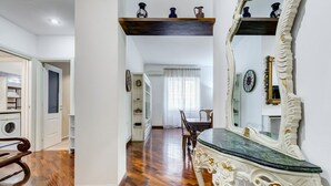 A room with a wooden floor, a dining table with chairs, a large mirror, and a shelf with decorative items. - L&L - Central charming 2-Bdr! (Roma)