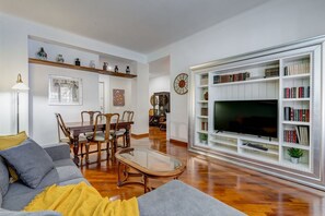 Una sala de estar con sofá, mesa de centro, televisor, estantería y comedor.