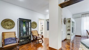 A room with wooden flooring, a black cabinet with glass doors, two wooden chairs, and a bed with ornate bedding. - L&L - Central charming 2-Bdr! (Roma)