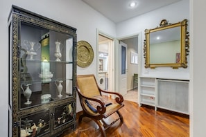 Una habitación con una silla de madera, un aparador de vidrio con objetos decorativos, un espejo grande y una chimenea.