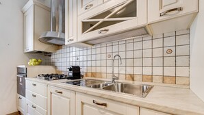 A kitchen with white cabinets, a stainless steel sink, and a tiled backsplash. - L&L - Central charming 2-Bdr! (Roma)