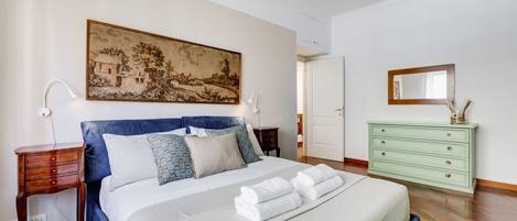 Un dormitorio con cama, mesita de noche, cómoda, un cuadro y una puerta.