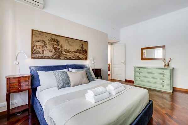 Un dormitorio con cama, mesita de noche, cómoda, un cuadro y una puerta.