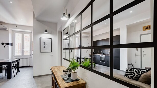 Un intérieur moderne comprenant un coin repas, une console en bois agrémentée d’une plante et une cuisine visible à travers une grande fenêtre.