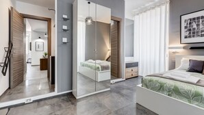 Une chambre à coucher moderne avec un grand miroir, un lit recouvert d’une couvre-lit à motifs de feuilles vertes, une table de chevet et une commode.