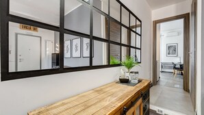 Un couloir avec une console en bois, un miroir à cadre noir et des œuvres d’art encadrées accrochées au mur.