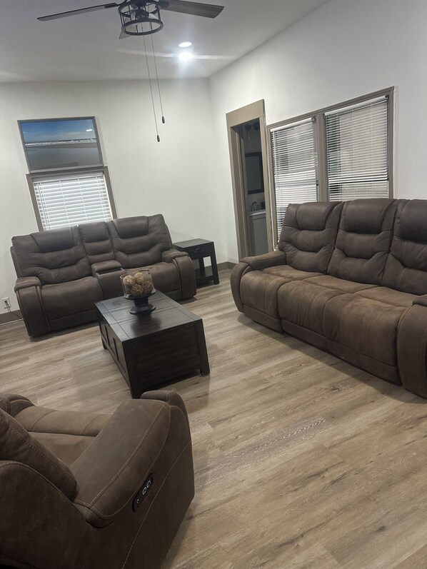 A modern living room with two brown leather sofas, a wooden coffee table, and a ceiling fan.