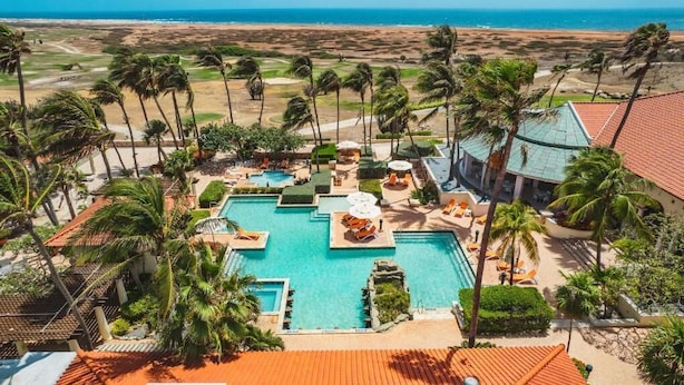 A resort with multiple swimming pools, palm trees, and a view of the beach. - Tierra del Sol Beach Home (Noord)