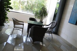A room with a tiled floor, a table, and four chairs. There is a potted plant and a painting on the wall. - Q+ · Beihai Beibu Bay No.1 Yijia Online Serviced Apartment (Beihai)