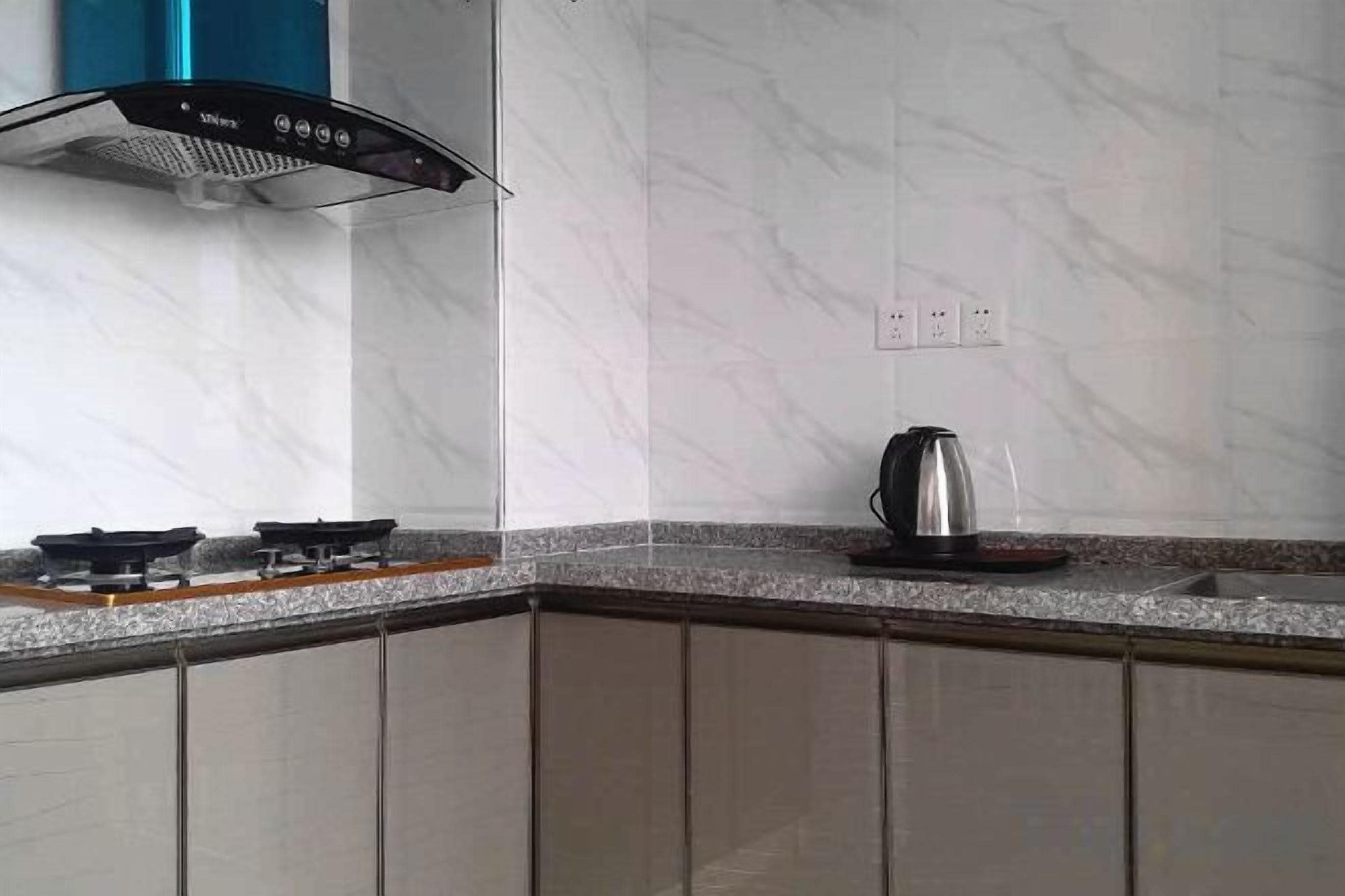 A kitchen with a gas stove, a kettle, and a modern range hood.