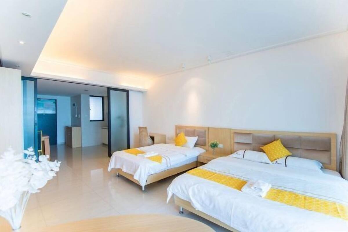Una habitación de hotel moderna con dos camas, un televisor y una puerta de vidrio que da a un pasillo.