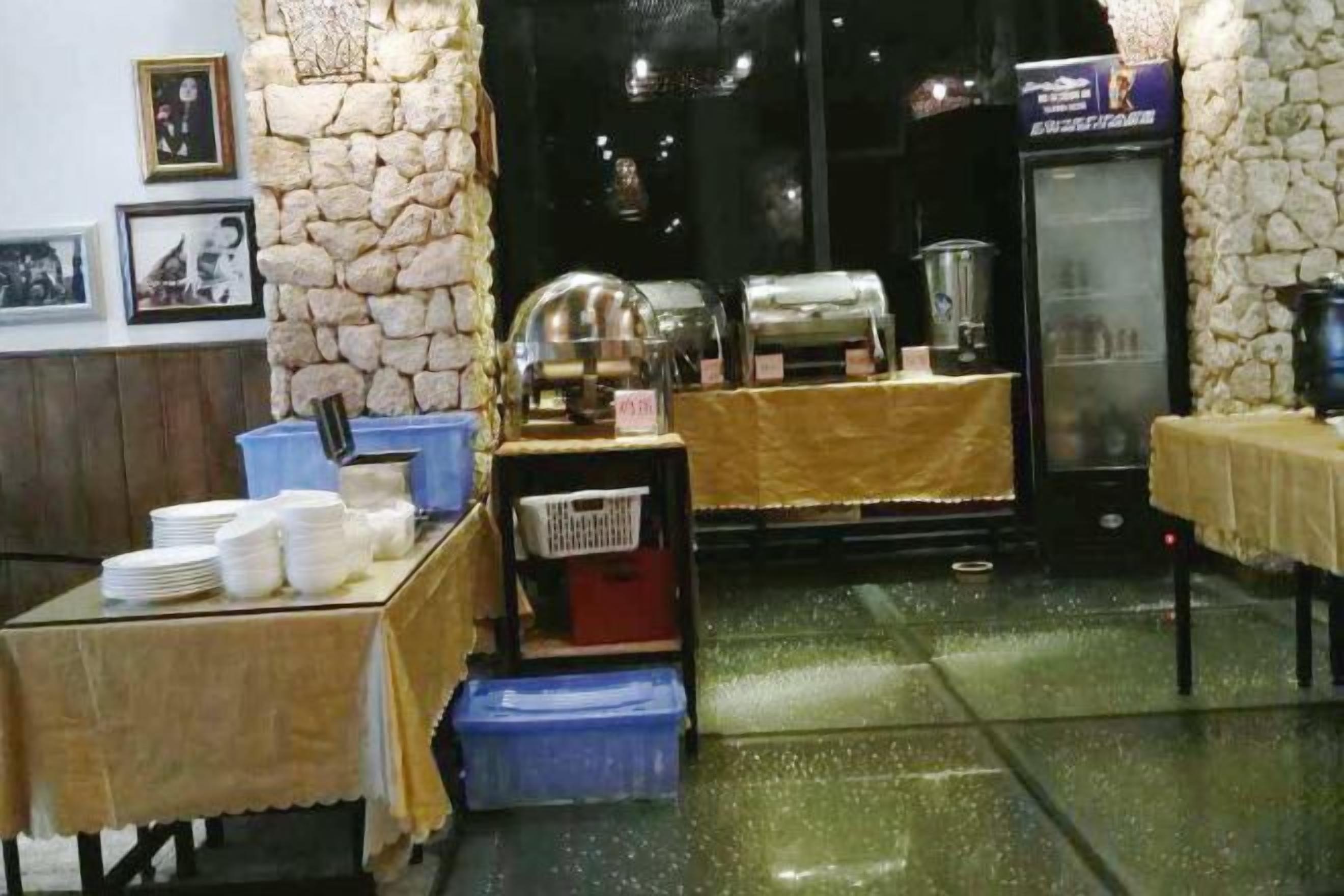 A restaurant interior with a stone wall, buffet setup, and a refrigerator.