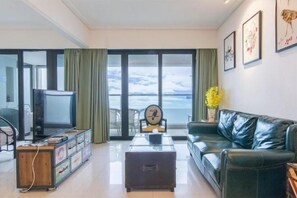 A living room with a television, a sofa, a coffee table, and a view of the sea through large windows. - Q+ · Beihai Beibu Bay No.1 Yijia Online Serviced Apartment (Beihai)