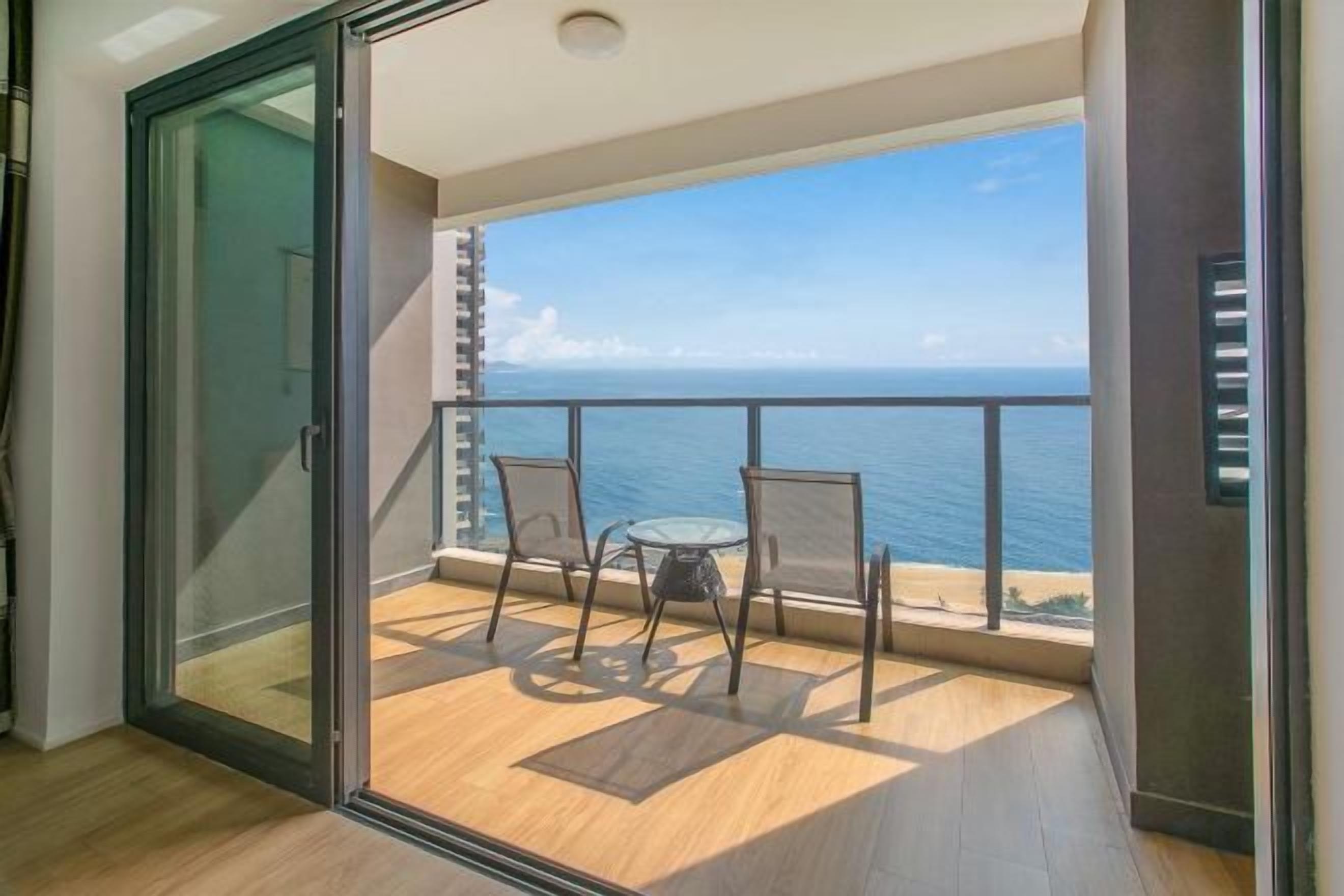 A balcony with a glass door, a table, two chairs, and a view of the ocean.
