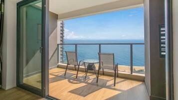 A balcony with a glass door, a table, two chairs, and a view of the ocean.
