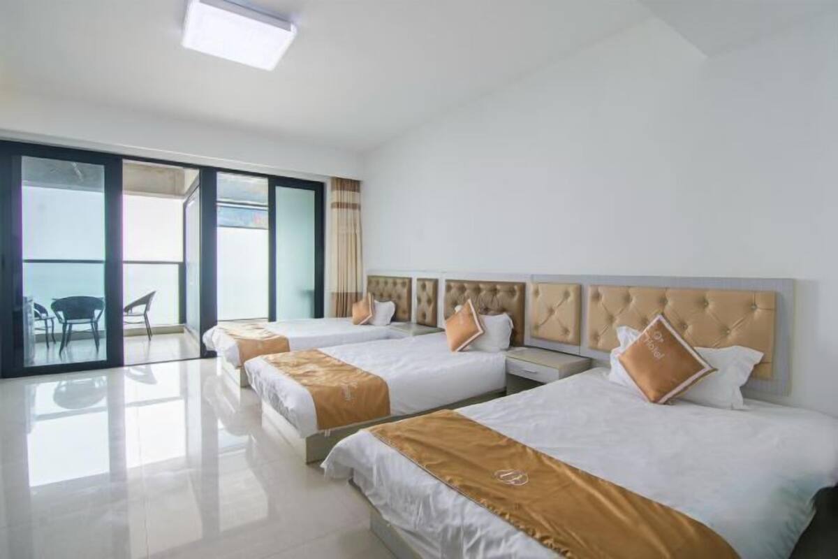 Habitación de hotel con tres camas, un amplio ventanal corredero que da a un balcón y un diseño moderno.