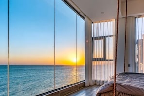 Una stanza con una grande finestra vista mare, un letto e un'altalena in corda.