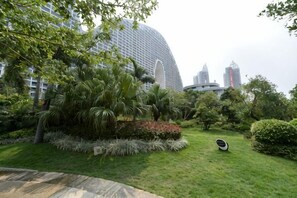 A landscaped garden with palm trees and shrubs, a curved pathway, and modern buildings in the background. - Q+ · Beihai Beibu Bay No.1 Yijia Online Serviced Apartment (Beihai)