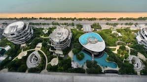 A high-rise hotel with multiple circular balconies, a central swimming pool, and a view of the beach.