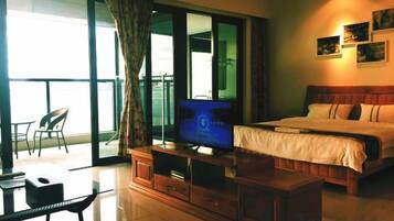 A hotel room with a bed, a television, a wooden cabinet, a balcony with a chair, and a view of the sea.