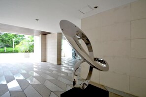 Ein modernes Interieur mit einer geometrischen Metallskulptur, Fliesenböden und Blick auf Grünflächen im Freien.