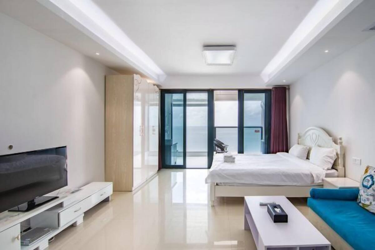 Una habitación de hotel moderna con una cama grande, televisión, sofá y balcón con vistas.