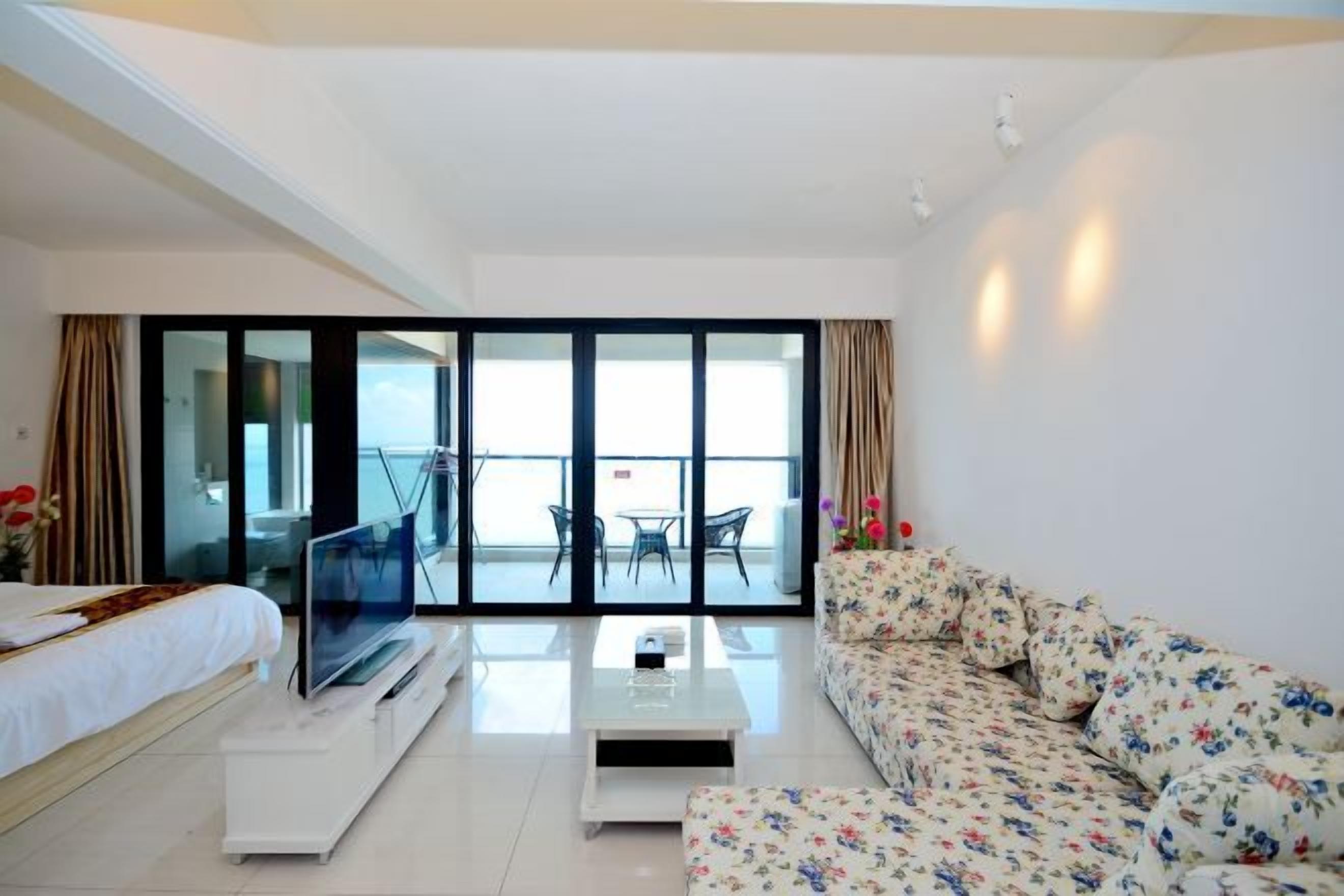 A hotel room with a bed, a TV, a sofa, a coffee table, and a balcony with a view.