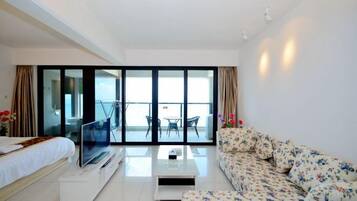A hotel room with a bed, a TV, a sofa, a coffee table, and a balcony with a view.