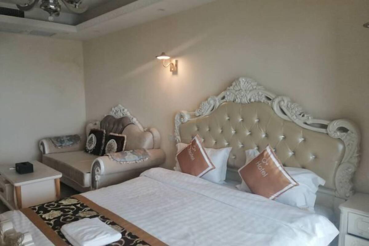 Una habitación de hotel con una cama grande, un sofá, una mesita de noche y una lámpara de pared.