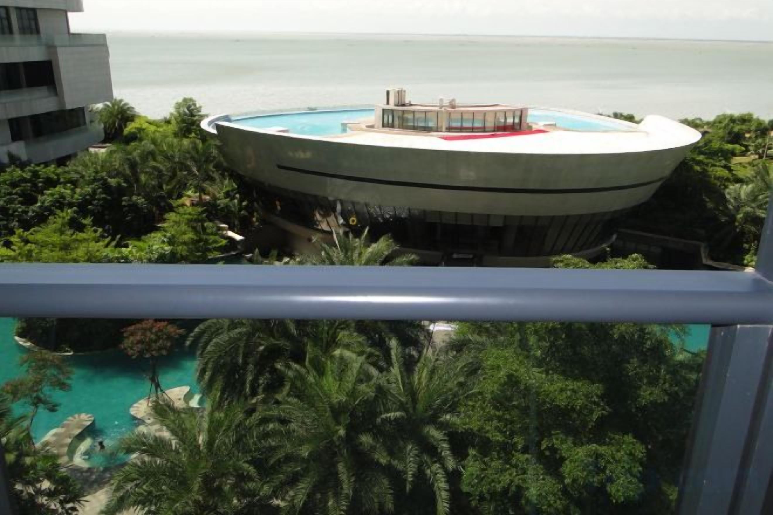 A circular building with a pool, surrounded by greenery and overlooking a body of water.