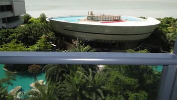 A circular building with a pool, surrounded by greenery and overlooking a body of water.