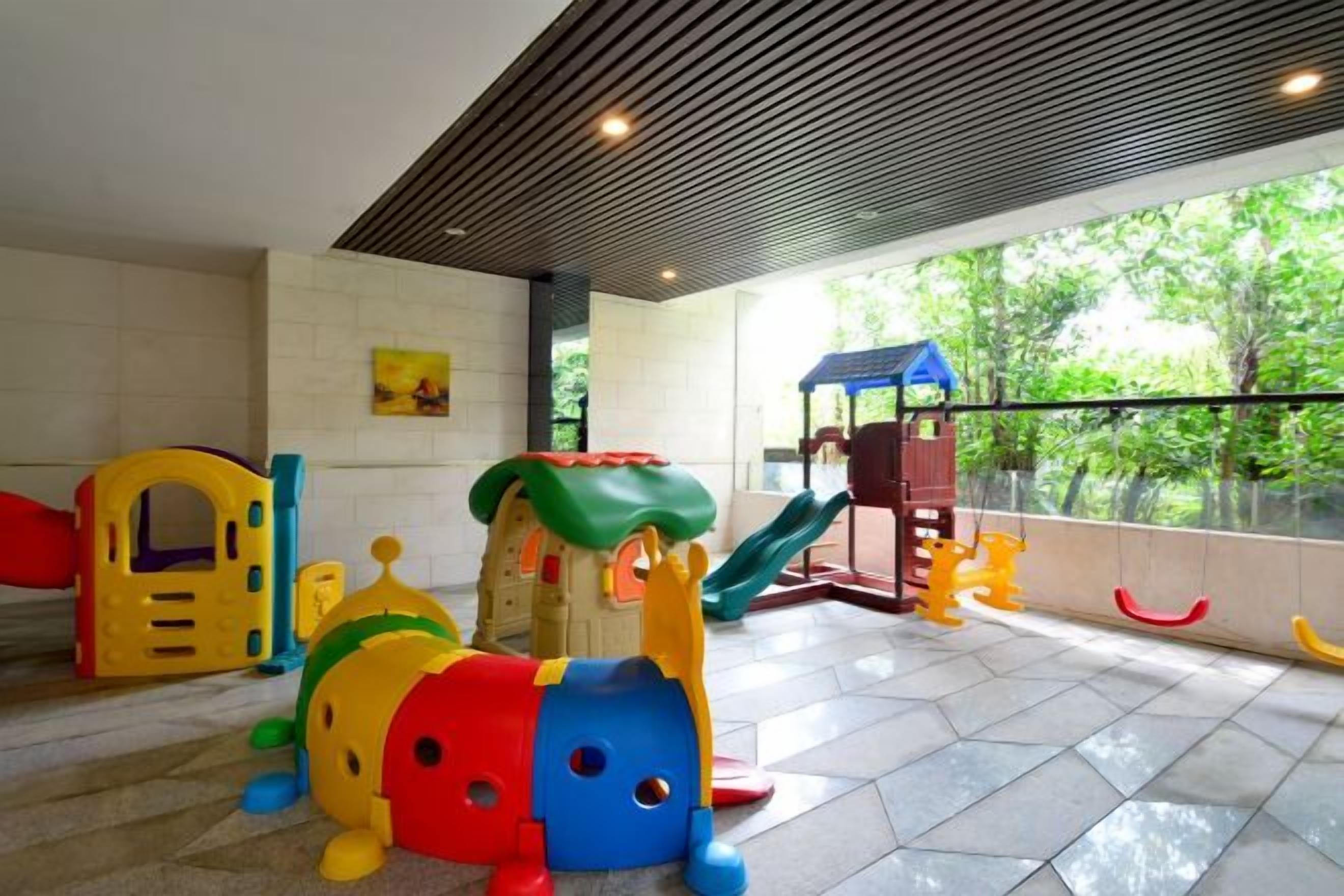 A children's play area with various play structures, a slide, and a view of greenery outside.