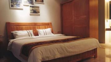 Cama com cabeceira de madeira, roupa de cama branca e manta estampada.