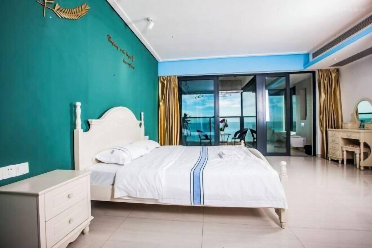 Un dormitorio con cama, cómoda, escritorio y vista al mar a través de un ventanal.