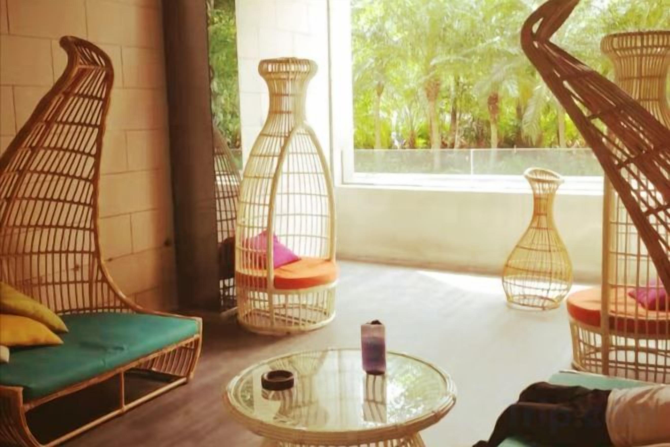 A room with wicker furniture, a glass table, and a view of greenery outside.