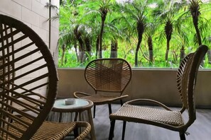 A room with wicker chairs and a small table, a large window with a view of green trees. - Q+ · Beihai Beibu Bay No.1 Yijia Online Serviced Apartment (Beihai)