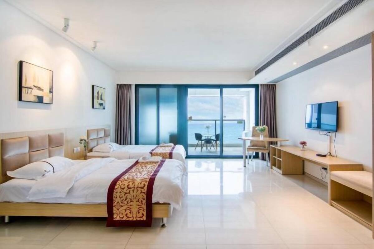 Habitación de hotel con dos camas, televisión, escritorio y balcón con vistas.