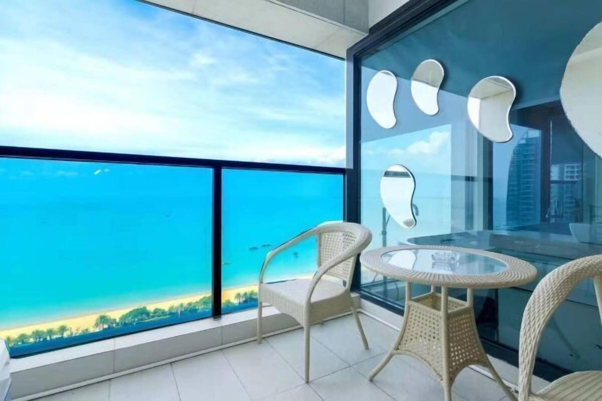 Un balcón con una mesa de vidrio y sillas de mimbre, con vistas a un cielo azul despejado y un paisaje lejano.