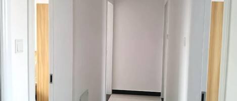 Um corredor estreito com paredes brancas e uma porta de madeira à direita.