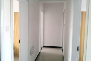 Un couloir étroit aux murs blancs, avec une porte en bois sur le côté droit.