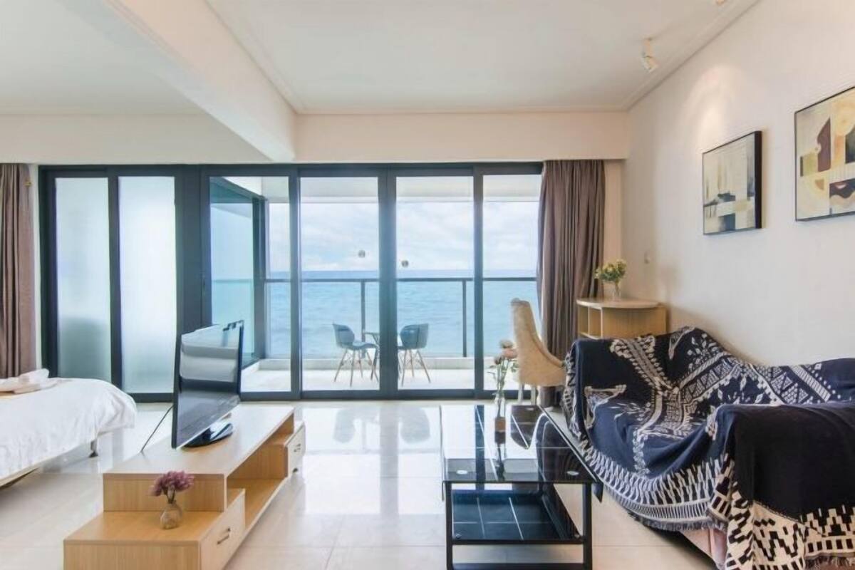 Una habitación de hotel moderna con un balcón amplio, un sofá, un televisor y un comedor.