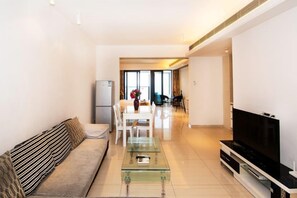 A modern living room with a sofa, a glass coffee table, a flat-screen TV, and a dining area in the background. - Q+ · Beihai Beibu Bay No.1 Yijia Online Serviced Apartment (Beihai)