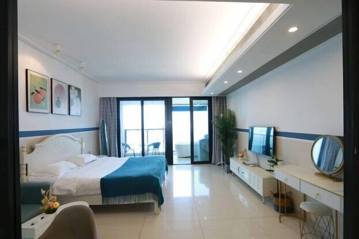Habitación de hotel con cama, escritorio, silla, televisor y balcón con vistas.