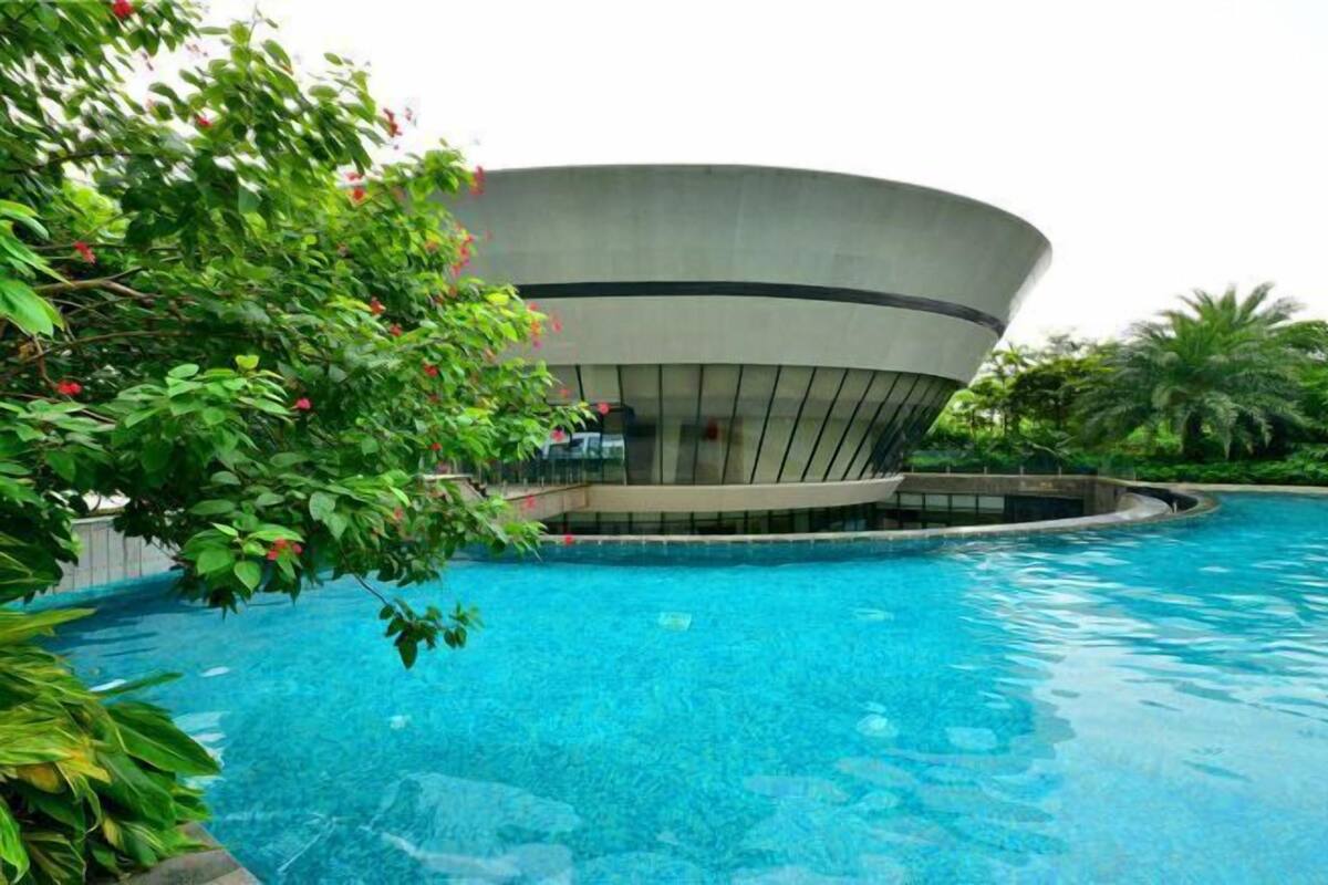 Un edificio moderno con techo curvo, piscina y abundante vegetación.