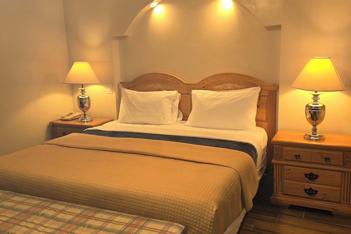 A hotel room with a large bed, two bedside tables with lamps, a bench, and a wooden floor.
