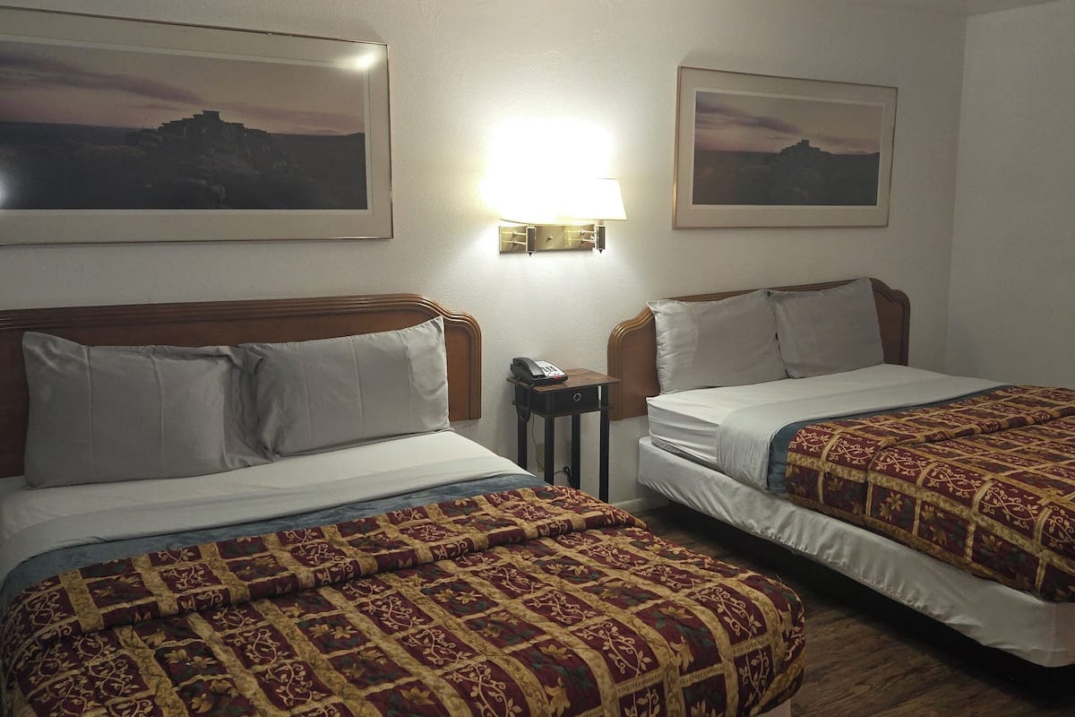 A hotel room with two beds, each with a patterned bedspread, a bedside table with a lamp, and framed pictures on the wall.