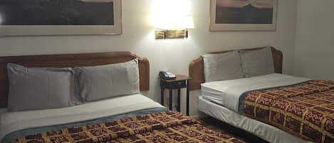 A hotel room with two beds, each with a patterned bedspread, a bedside table with a lamp, and framed pictures on the wall.