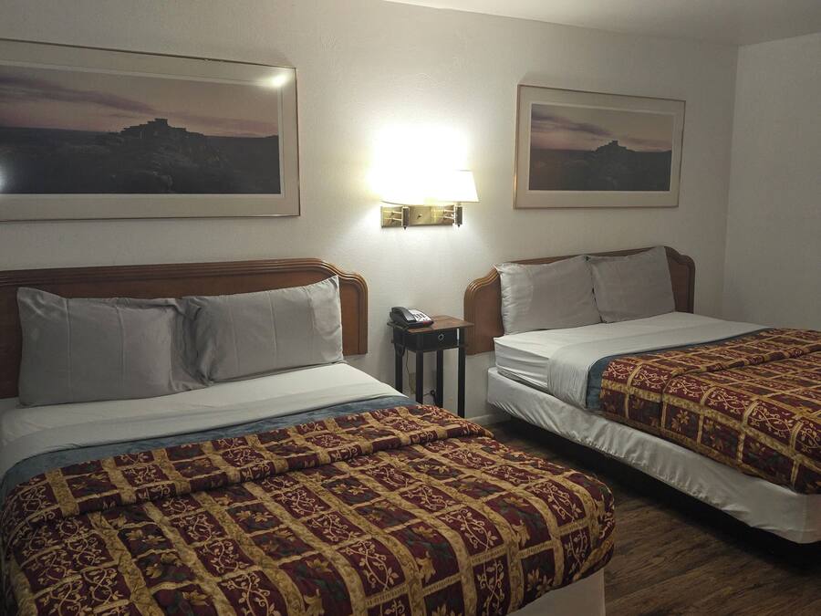 Habitación de hotel con dos camas, cada una con una colcha estampada, una mesita de noche con lámpara y cuadros enmarcados en la pared.