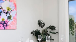 A dining area with a wooden table set for four, white chairs, and a large floral painting on the wall. - Kismet- Family fav, 12pm check out, Parking, Walk to the beach (Ocean Grove)