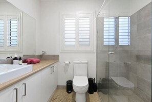Ein modernes Badezimmer mit Toilette in Weiß, einer Duschkabine aus Glas und einem beige gefärbten Waschtisch mit Waschbecken und Toilettenartikeln.